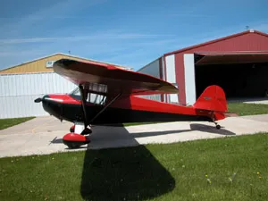 A red and black plane parked in front of a hangar.