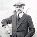 A man in suit and hat standing next to an airplane.
