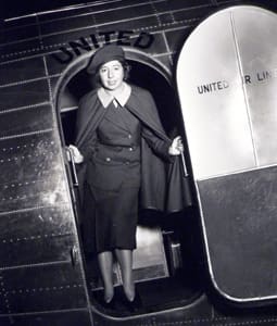 A woman in an old photo standing inside of a plane.