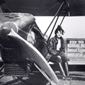 A woman sitting on the ground next to an airplane.