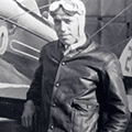 A man in leather jacket and goggles standing next to an airplane.