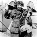 A woman in a black and white photo holding two helmets.