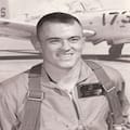 A man in an air force uniform with a plane behind him.